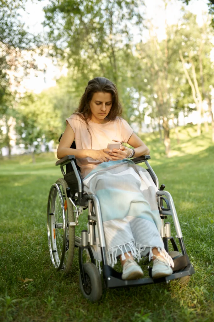 Disabled woman in wheelchair using mobile phone in park. Paralyzed people and disability, handicap overcoming. Handicapped female person walking in park